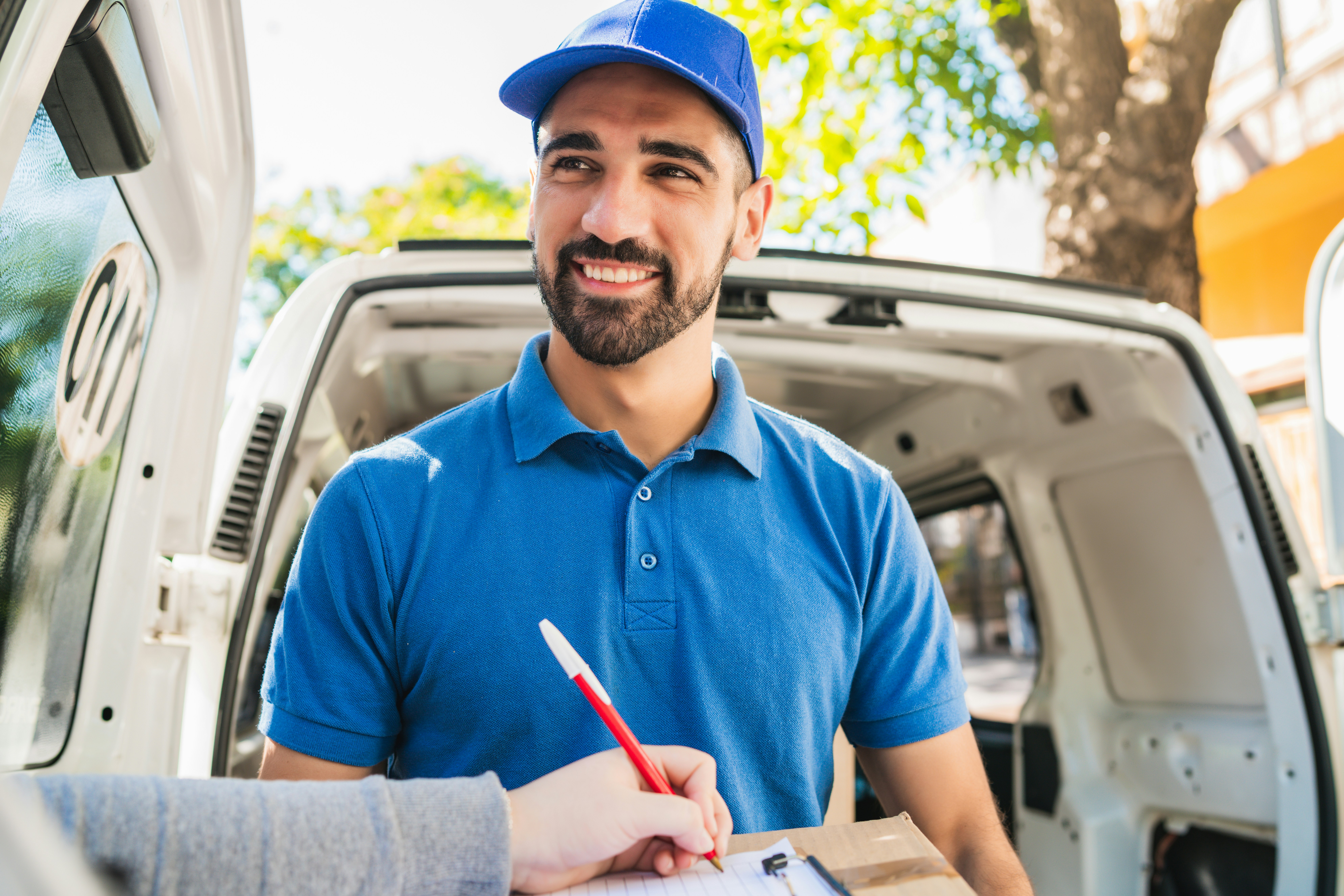 Courier beside a delivery van as a customer signs for a package outdoors